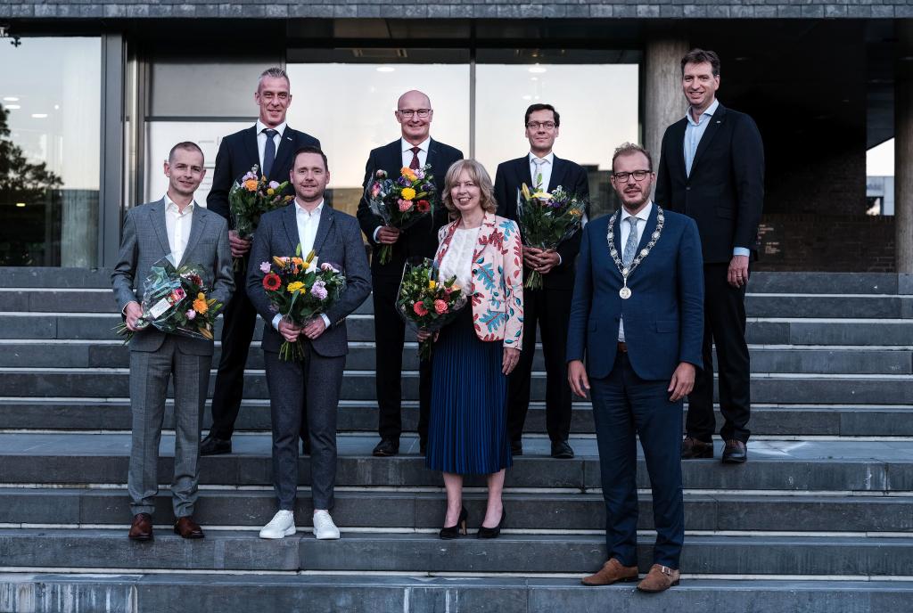 De burgemeester, wethouders en gemeentesecretaris staan op de trap voor het stadhuis